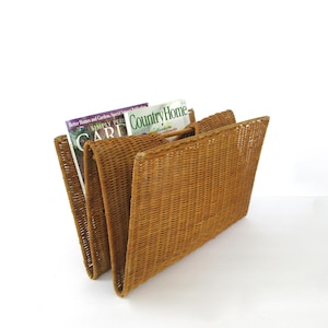 May include: A brown woven wicker magazine rack with a folding design. The rack features a textured, natural fiber construction and contains two magazines, one titled Country Home and another partially visible with the text Simply Garden.