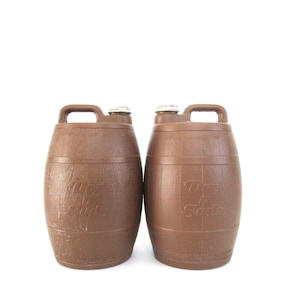 May include: Two brown plastic barrels with handles and screw-on lids. The barrels have a wood-grain texture and the text "Milo's Soda" is printed on the front. The barrels are on a white background.
