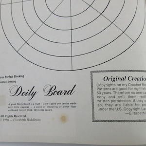 K&ouml;nnte beinhalten: Ein Schwarzwei&szlig;bild einer Seite aus einem H&auml;kelbuch. Die Seite zeigt ein Diagramm eines Doily-Bretts, das zum Blocken von geh&auml;kelten Doilies verwendet wird. Der Text auf der Seite lautet "Doily Board" und "Assures Perfect Blocking" und "Eliminates Ironing". Die Seite enth&auml;lt auch einen Copyright-Hinweis und Informationen &uuml;ber die Autorin des Buches, Elizabeth Hiddleson.