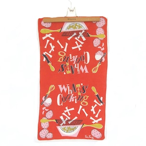 May include: A red kitchen towel with the words "What's Cooking" in white, along with illustrations of cooking utensils and food items. The towel is hanging on a wooden hanger.