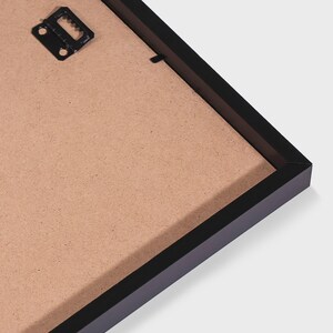 May include: The back of a black rectangular picture frame featuring a brown fiberboard backing. A black metal sawtooth hanger is attached to the upper left corner of the frame, providing a secure point for wall mounting the display item.