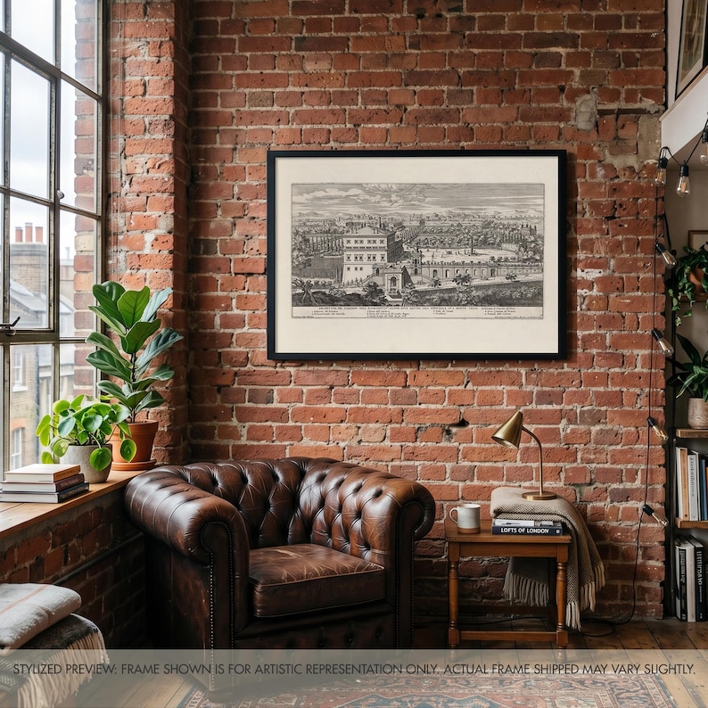 May include: A black and white architectural print in a thin black frame depicting a historical landscape with buildings and gardens, featuring detailed line work and text at the bottom, displayed on a rustic red brick wall above a leather chair.