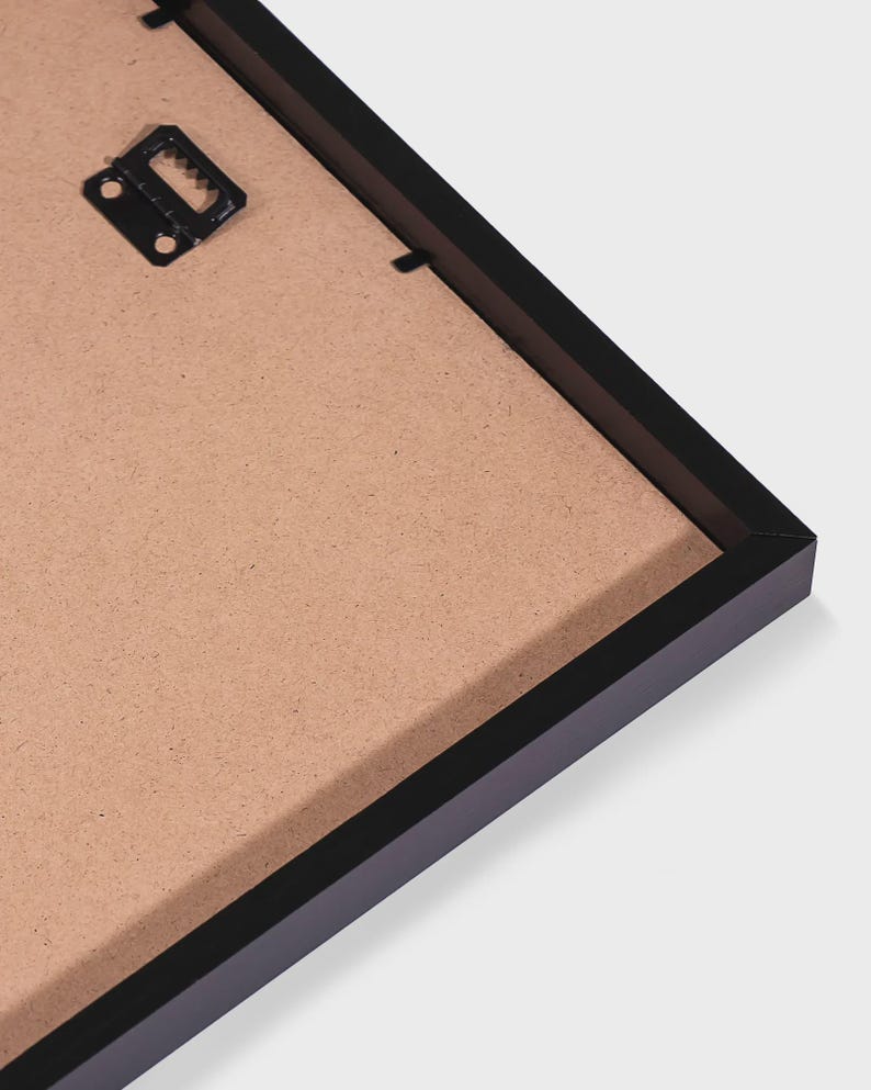 May include: The back of a black rectangular picture frame featuring a brown fiberboard backing. A black metal sawtooth hanger is attached to the upper left corner of the frame, providing a secure point for wall mounting the display item.