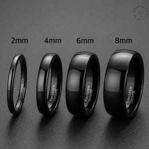 Op de afbeelding: Vier gepolijste zwarte wolfraamcarbide ringen op een rij, gelabeld met breedtes van 2mm, 4mm, 6mm en 8mm. Elke ring heeft een glad, gewelfd oppervlak en is gegraveerd met de tekst TUNGSTEN CARBIDE op de binnenkant van de band.