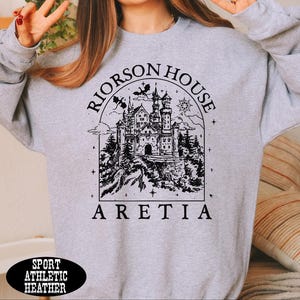 A person wearing a gray sweatshirt with a graphic design of a castle and the text "Riorson House Aretia" printed on it.