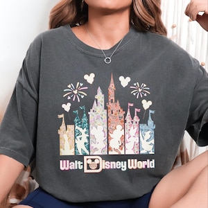 A person wearing a gray t-shirt with a graphic design featuring Disney World-themed elements such as a castle, Mickey Mouse, and fireworks.