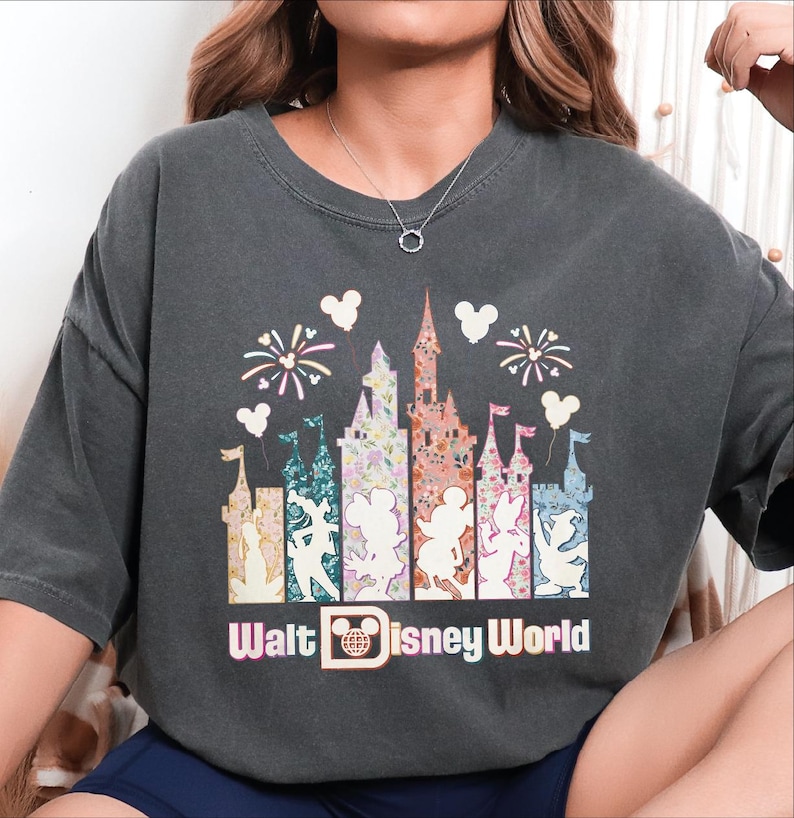 A person wearing a gray t-shirt with a graphic design featuring Disney World-themed elements such as a castle, Mickey Mouse, and fireworks.