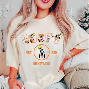 A woman wearing a white t-shirt with a graphic of Goofy and Mickey Mouse, along with text that says "Est. 1932 Disneyland".