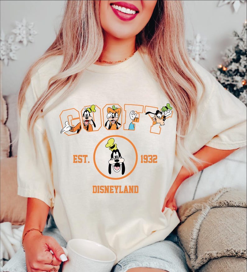A woman wearing a white t-shirt with a graphic of Goofy and Mickey Mouse, along with text that says "Est. 1932 Disneyland".