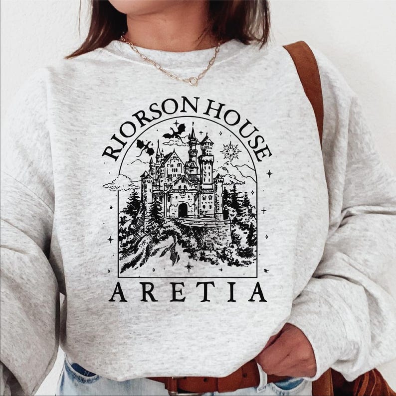A person wearing a gray sweatshirt with a graphic design depicting a castle and the text "Rierson House Areia" printed on it.