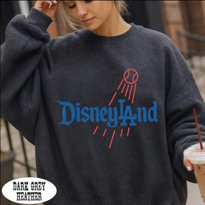 A woman wearing a gray sweatshirt with the word "Disneyland" printed on it, holding a drink in her hand.