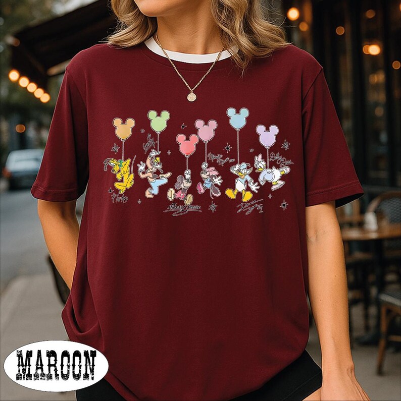 A woman wearing a burgundy t-shirt with a Disney character design, including Mickey Mouse, Donald Duck, and Goofy, along with balloons.