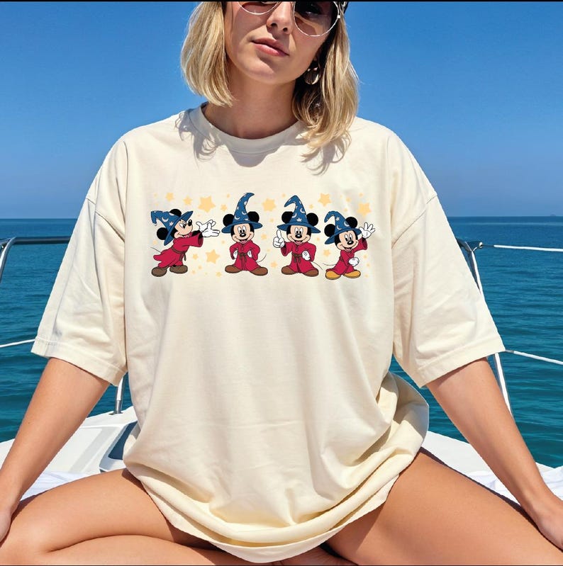 A woman wearing a white t-shirt with a graphic of Mickey Mouse characters on it, sitting on a boat with the ocean in the background.