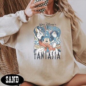 A person wearing a beige sweatshirt with a graphic of Mickey Mouse and the text "FANTASIA" printed on it.
