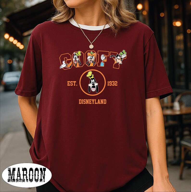 A woman wearing a burgundy t-shirt with a graphic of Goofy and Mickey Mouse, along with text that says "Est. 1932 Disneyland".