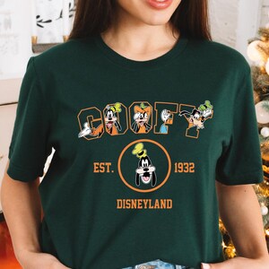 A woman wearing a green t-shirt with a graphic design featuring the characters Goofy and Mickey Mouse.