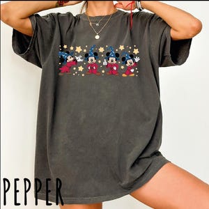 A person wearing a gray t-shirt with a graphic of Mickey Mouse and four other characters, along with stars and a red string.