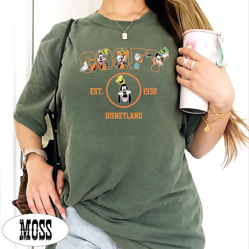A person wearing a green t-shirt with a graphic of Goofy and Mickey Mouse, holding a cup, and a necklace.