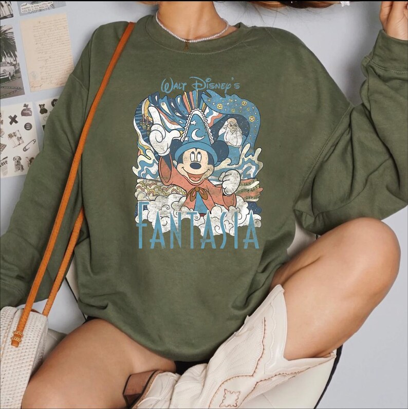 A person wearing a green sweatshirt with a Disney-themed graphic and text, including the character Mickey Mouse.