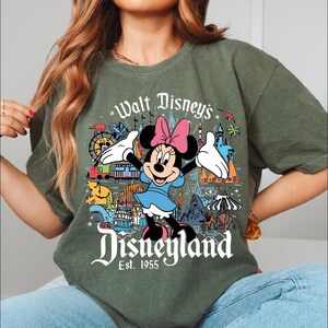 A woman wearing a green t-shirt with a graphic of Minnie Mouse and various Disney-themed illustrations.
