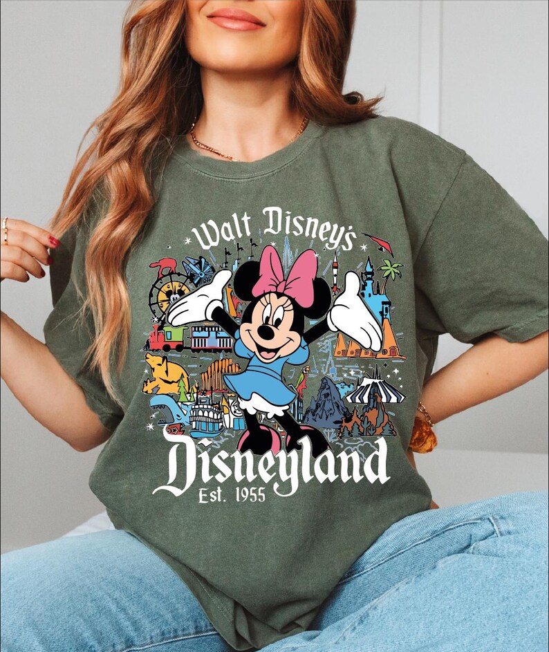 A woman wearing a green t-shirt with a graphic of Minnie Mouse and various Disney-themed illustrations.