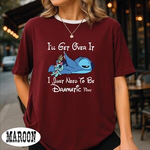 A person wearing a burgundy t-shirt with a cartoon character and text printed on it.