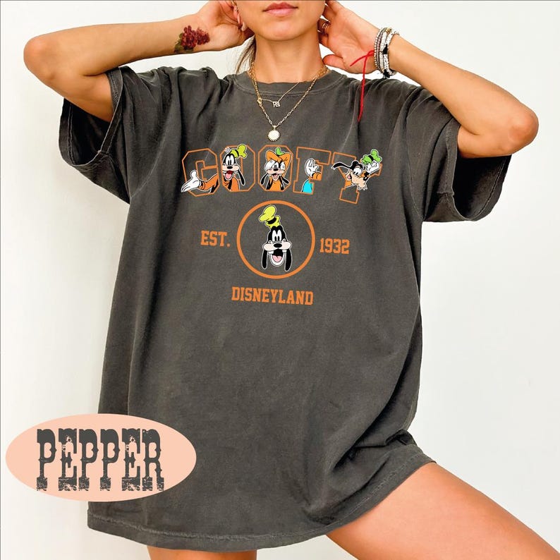 A person wearing a black t-shirt with a graphic of Goofy and Mickey Mouse, along with text that says "Est. 1932 Disneyland".