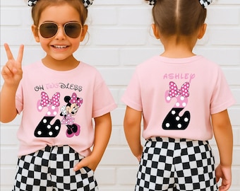 May include: A young girl wearing a pink t-shirt with a Minnie Mouse graphic and the text "Oh Two-Dless". The shirt features a large number "2" with a polka dot design. She is also wearing black and white checkered shorts.