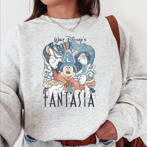A person wearing a gray sweatshirt with a Disney-themed graphic design featuring Mickey Mouse and the title "Fantasia".