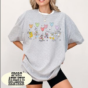 A woman wearing a gray sweatshirt with a graphic of Disney characters and balloons printed on it.
