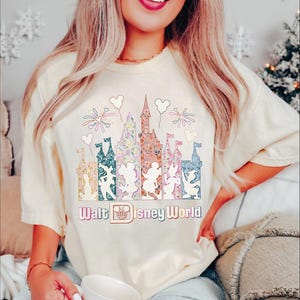 A woman wearing a white t-shirt with a Disney World-themed graphic and text, smiling and holding a cup.
