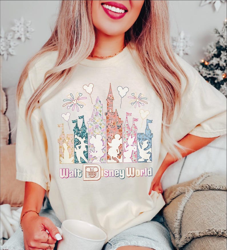 A woman wearing a white t-shirt with a Disney World-themed graphic and text, smiling and holding a cup.