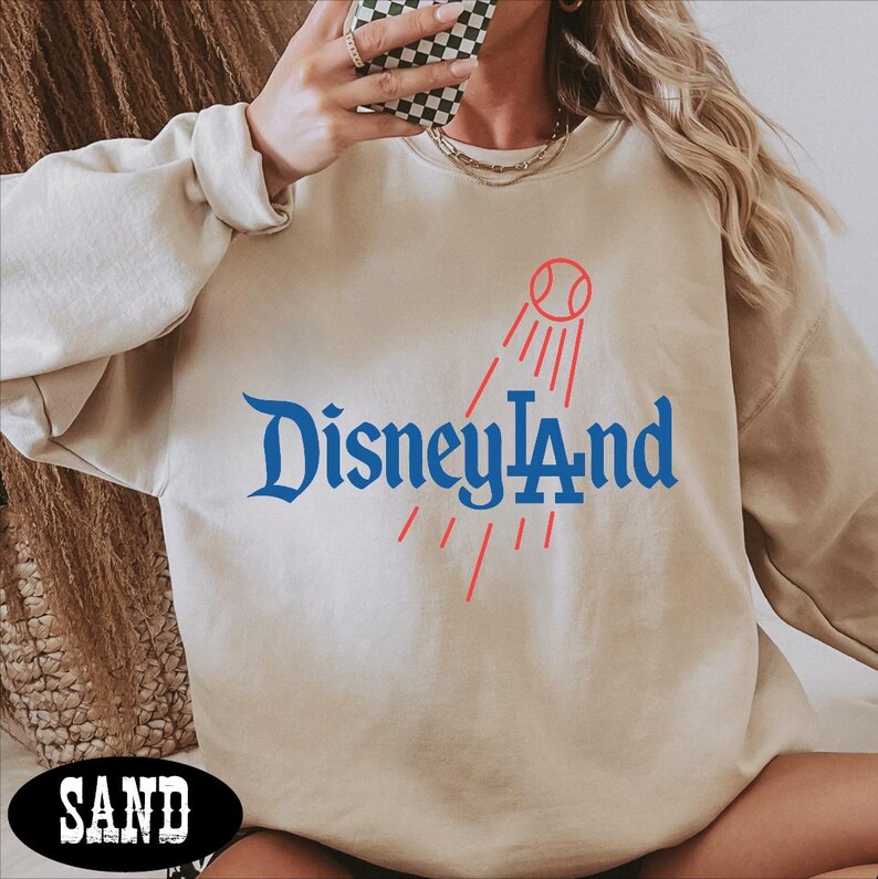 A person wearing a beige sweatshirt with the text "Disneyland" printed on it, holding a phone up to their face.