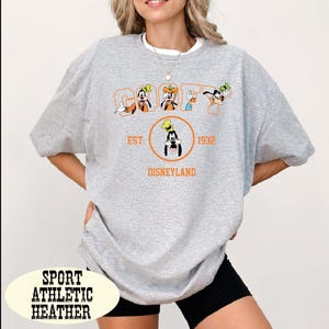 A woman wearing a gray t-shirt with a graphic design featuring Goofy and other Disney characters, along with text that says "Disneyland EST 1932 DISNEYLAND".