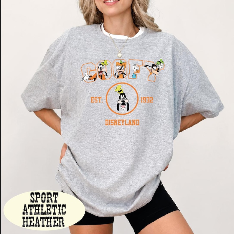 A woman wearing a gray t-shirt with a graphic design featuring Goofy and other Disney characters, along with text that says "Disneyland EST 1932 DISNEYLAND".