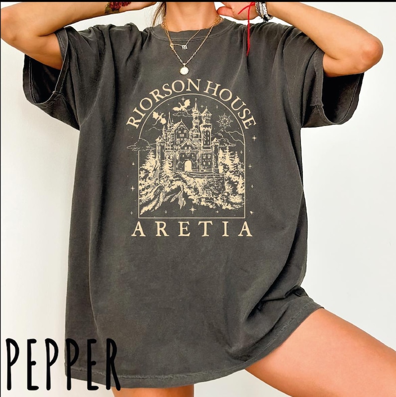 A person wearing a gray t-shirt with a graphic design of a castle and the text "Riorson House Aretia" printed on it.