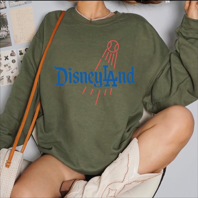 A person wearing a green sweatshirt with the Disney logo and a red baseball graphic, along with a white cowboy boot.