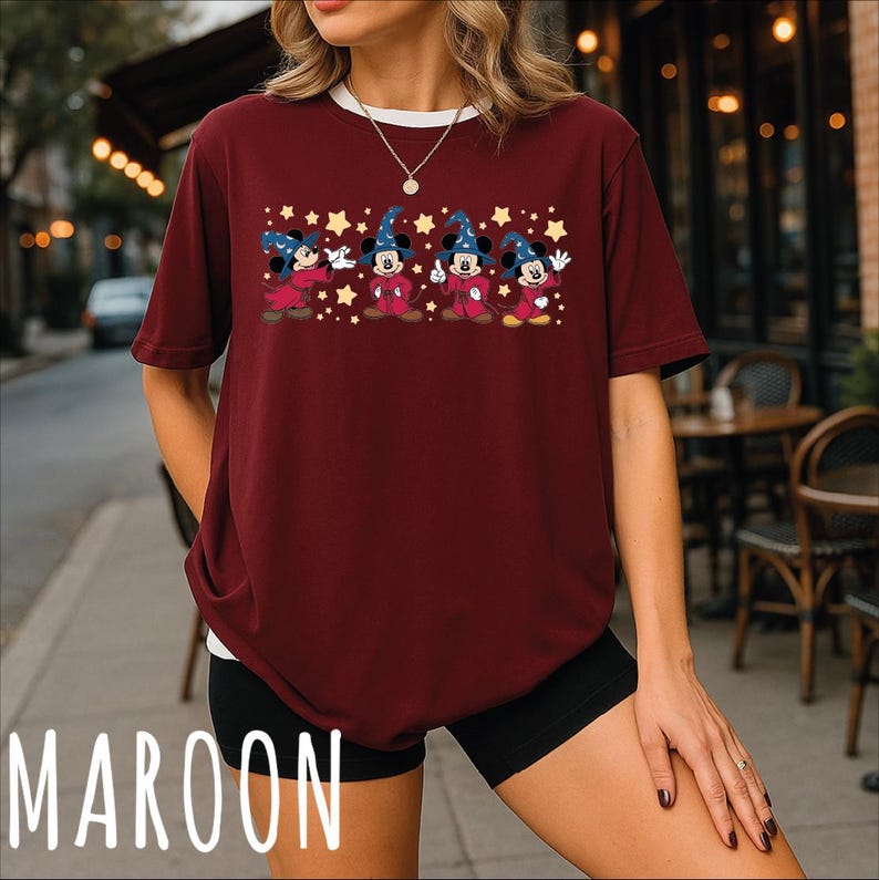 A woman wearing a maroon t-shirt with a graphic of Mickey Mouse and stars on it, standing on a city street.