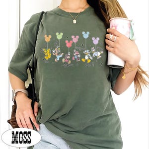 A person wearing a green t-shirt with a Disney character design and holding a cup.