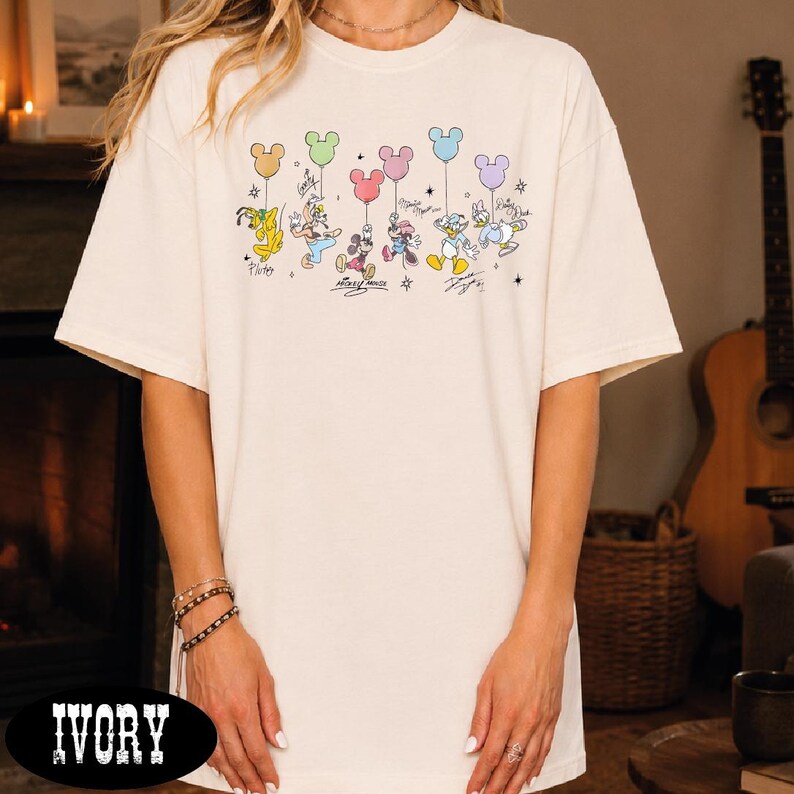 A person wearing a white t-shirt with a graphic of Disney characters and balloons printed on it.