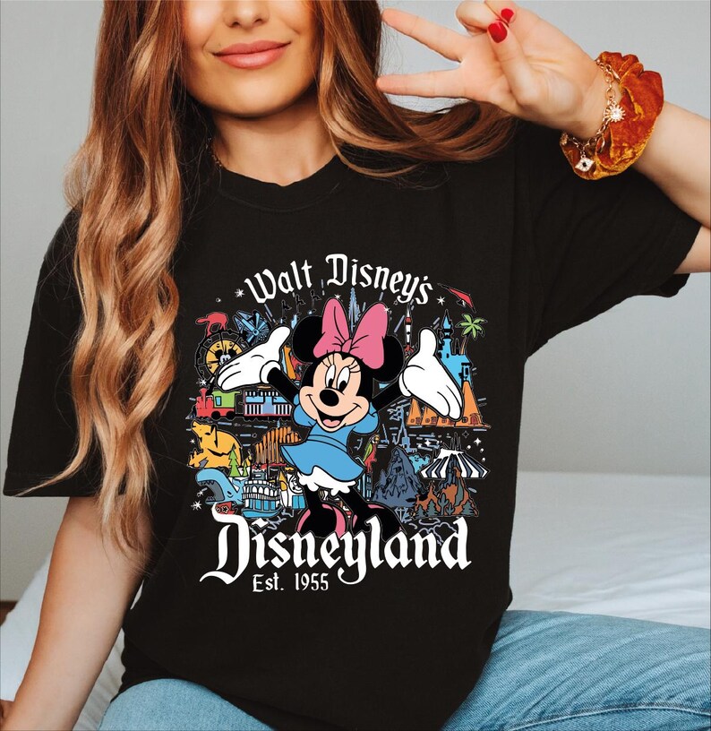 A woman wearing a black t-shirt with a Disney-themed graphic and text.