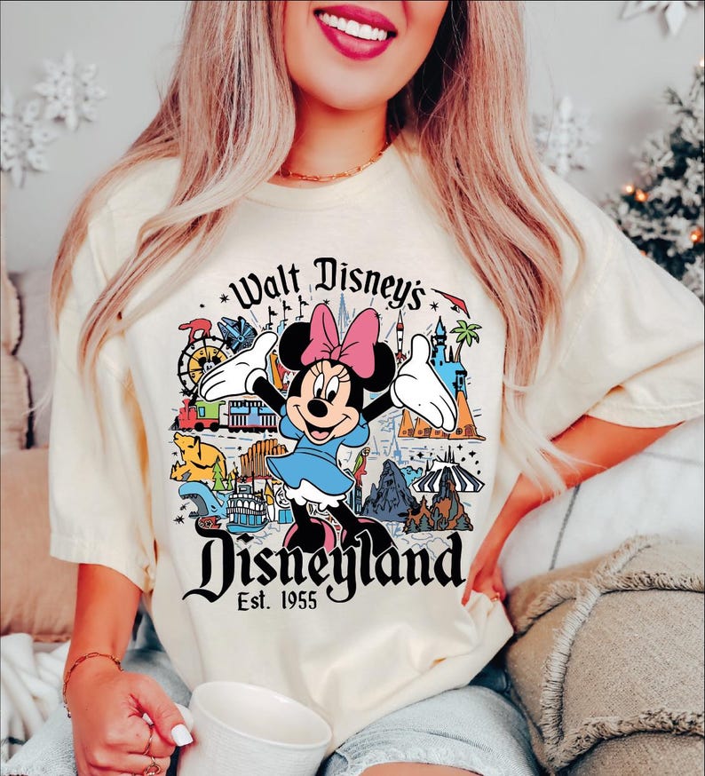 A woman wearing a white t-shirt with a Disney-themed graphic and text, smiling and holding a cup.