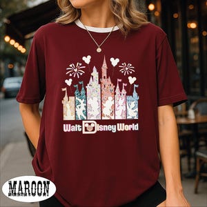 A woman wearing a burgundy t-shirt with a Disney World-themed graphic design, including a castle and fireworks.