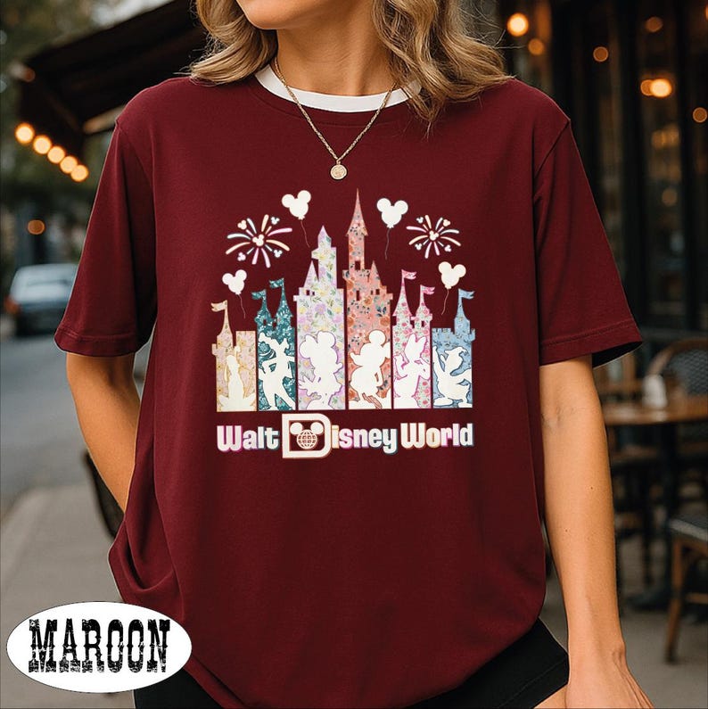 A woman wearing a burgundy t-shirt with a Disney World-themed graphic design, including a castle and fireworks.