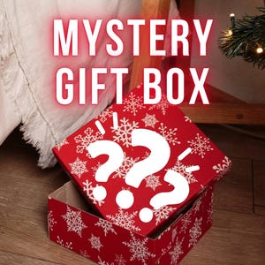 May include: A red gift box with white snowflakes and two large white question marks on the lid. The words "MYSTERY GIFT BOX" are displayed in large, white, glowing letters. The box is open, revealing an empty interior.