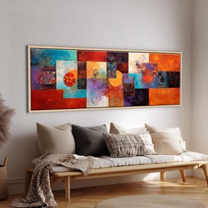 以下が含まれることがあります： 木製のフレームに入った抽象芸術作品。赤、オレンジ、青、紫の色合いで、カラフルな幾何学模様のコラージュが特徴です。木製のベンチの上に掛けられており、クッションと毛布が置かれています。