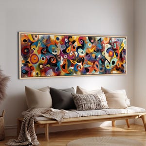 Puede incluir: Impresión en lienzo de arte abstracto con una vibrante mezcla de colores que incluyen naranja, azul, amarillo y morado. La obra presenta formas y patrones orgánicos, enmarcada en madera natural. La pintura cuelga sobre un banco de madera con cojines y una manta.
