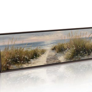 May include: A panoramic framed canvas print depicting a coastal scene with a wooden boardwalk path leading through sand dunes covered in tall grasses toward a calm blue ocean under a soft, light-filled sky at either sunrise or sunset.