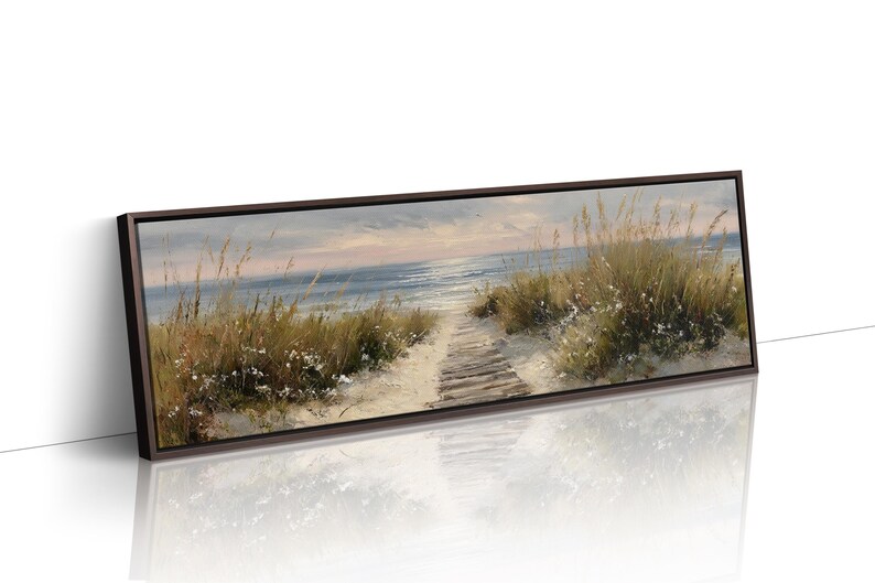 May include: A panoramic framed canvas print depicting a coastal scene with a wooden boardwalk path leading through sand dunes covered in tall grasses toward a calm blue ocean under a soft, light-filled sky at either sunrise or sunset.