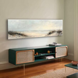 May include: A long, rectangular landscape painting depicting a coastal beach scene with soft, muted tones of beige, white, and pale blue. The artwork features sand dunes with tall grasses in the foreground and a calm ocean horizon in the distance.